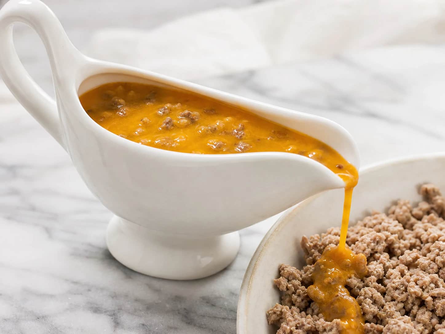 Silky orange pumpkin topper with tiny cooked beef crumbles in a porcelain sauce boat